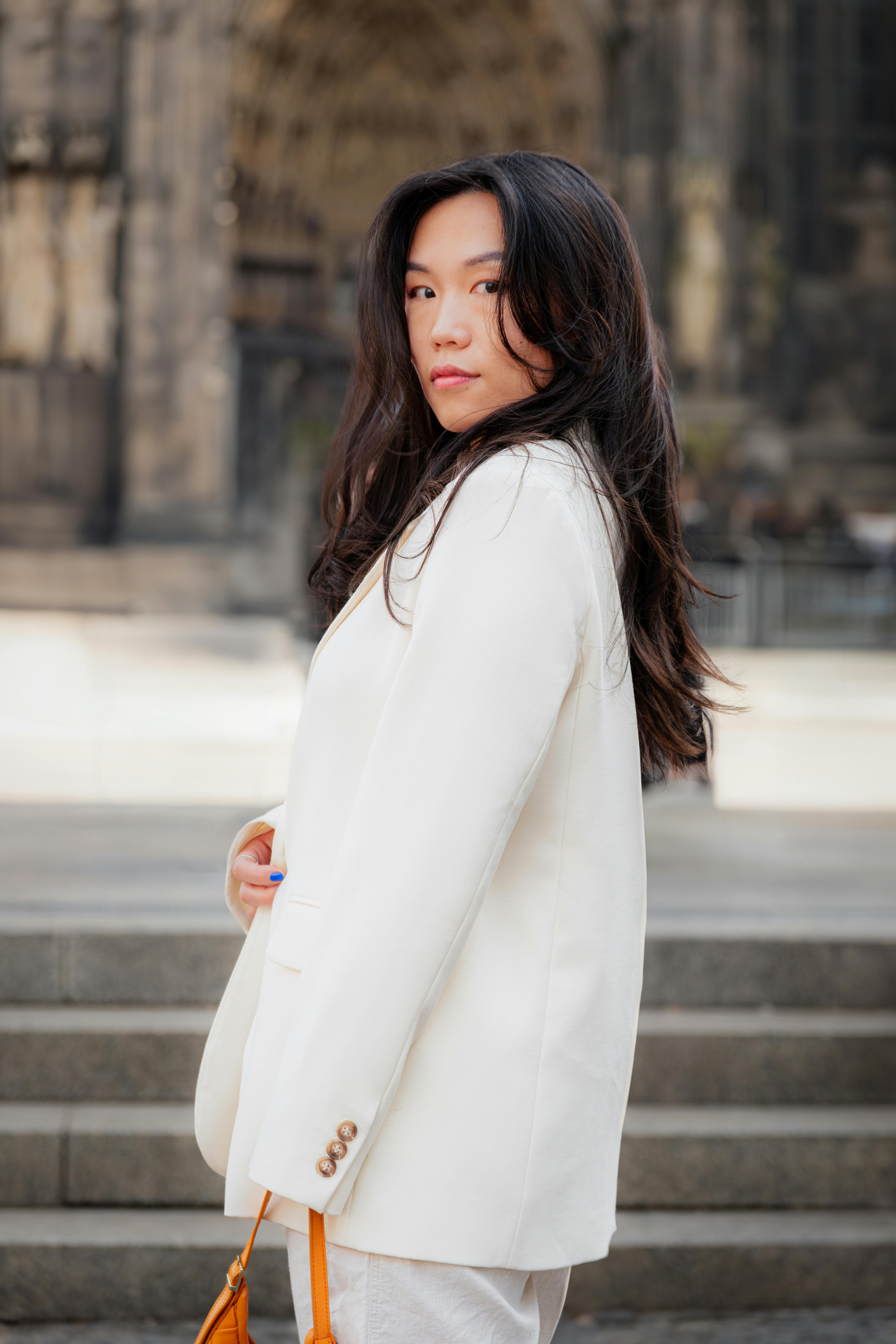Stylish woman poses in a white blazer outdoors in Cologne, Germany.