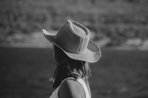 Free Black and white image of a woman wearing a cowboy hat looking at a serene water landscape. Stock Photo