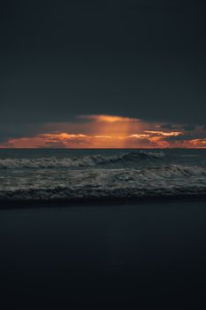 Dramatic ocean scene with waves and a vivid sunset, storm clouds overhead.