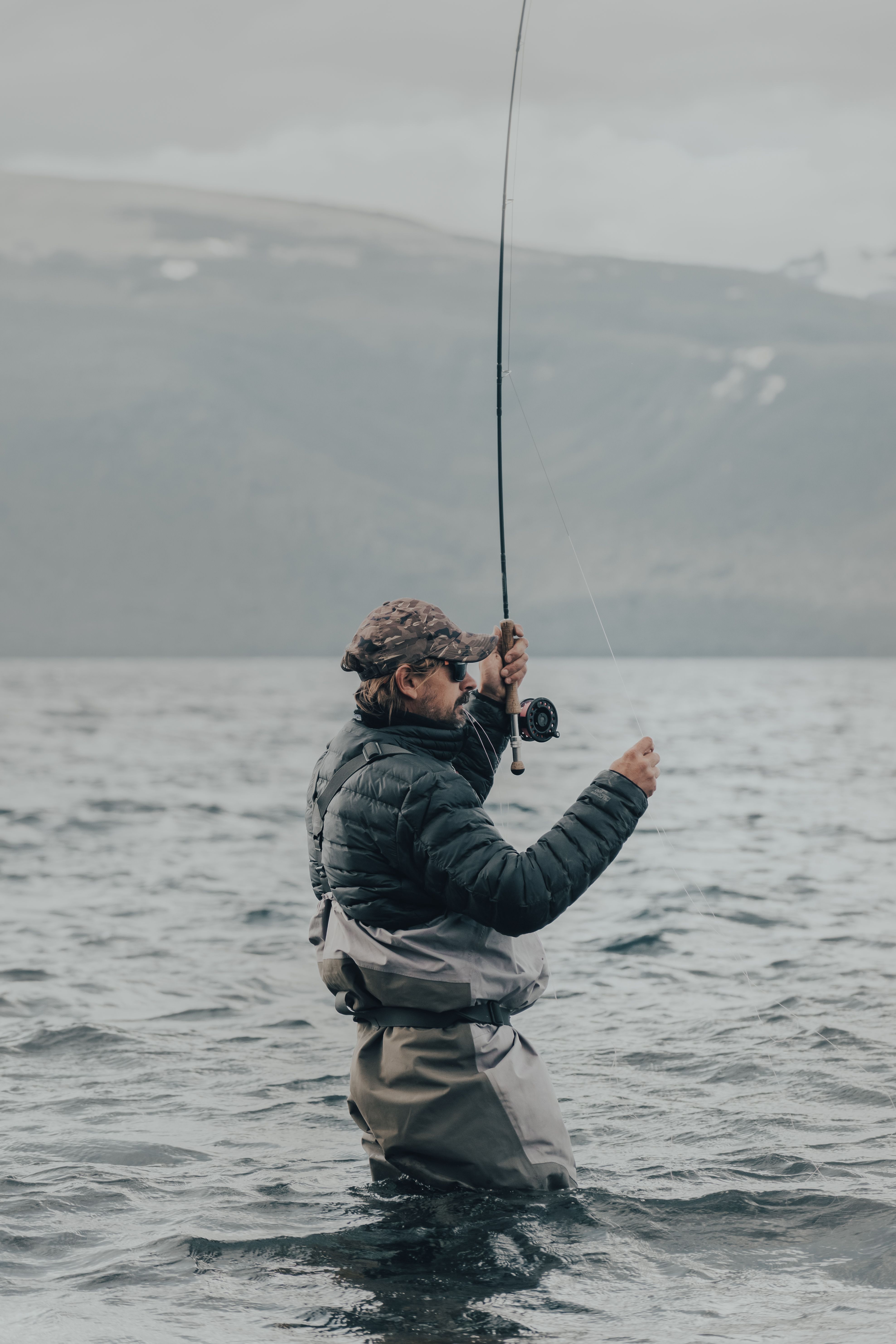A man engaged in fly fishing in a mist-covered bay, enjoying leisure time.