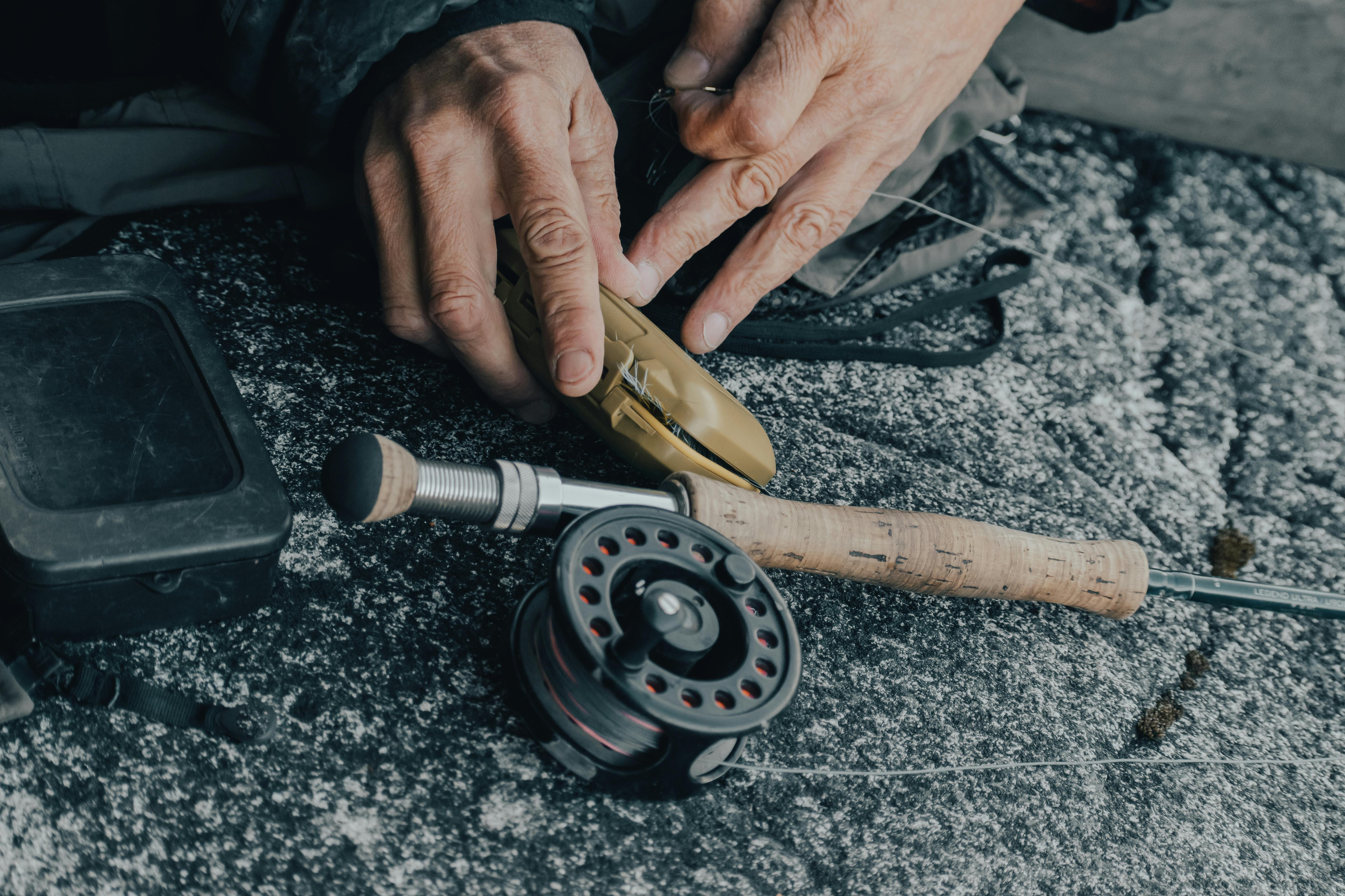 Detailed shot of fishing gear with hands preparing the equipment on a rocky surface outdoors.