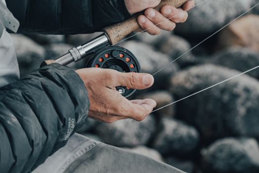 Detailed shot of a man holding a fishing rod, focusing on hands and reel in a natural setting.
