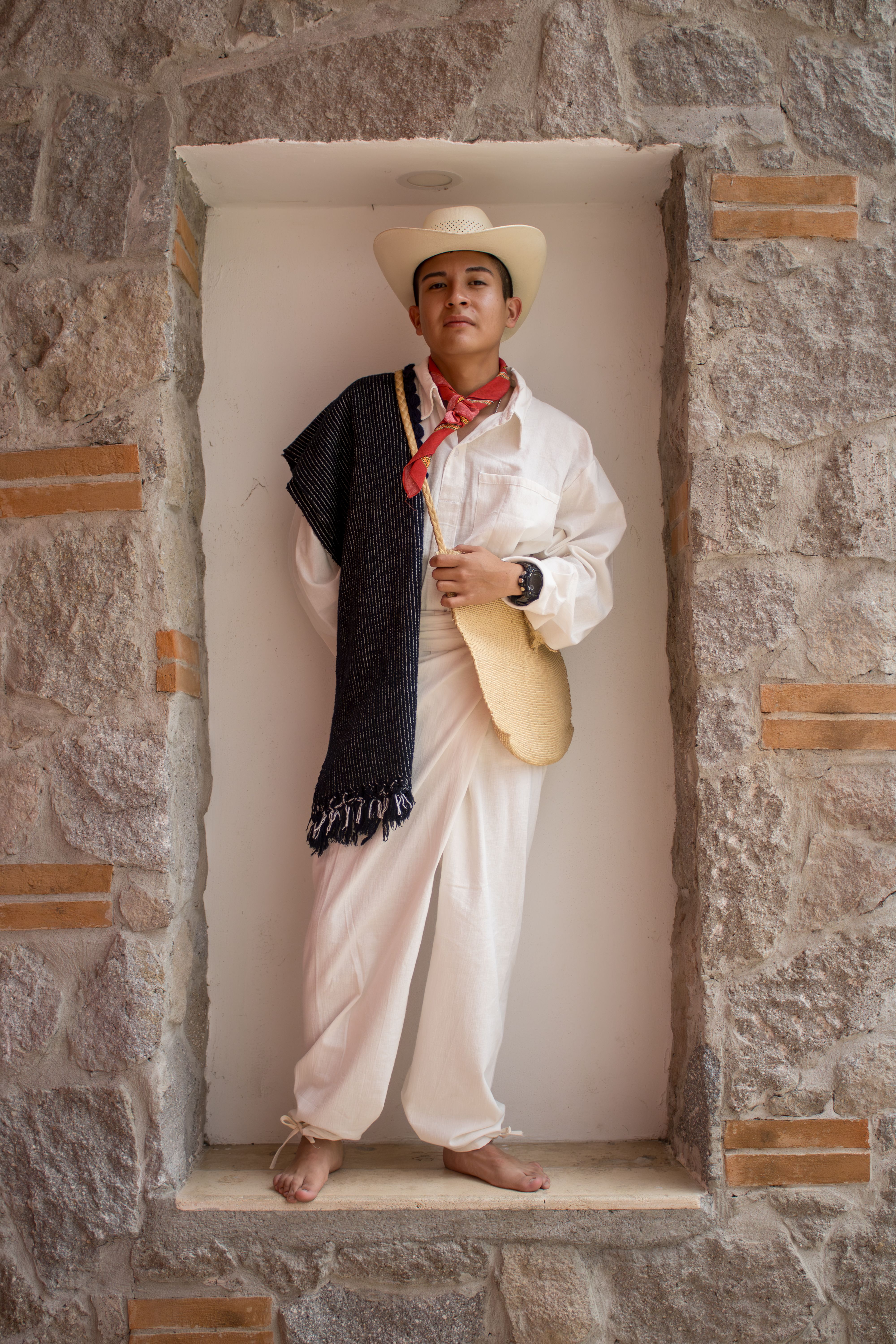 Man standing in niche wearing traditional Hispanic attire with cowboy hat and poncho.