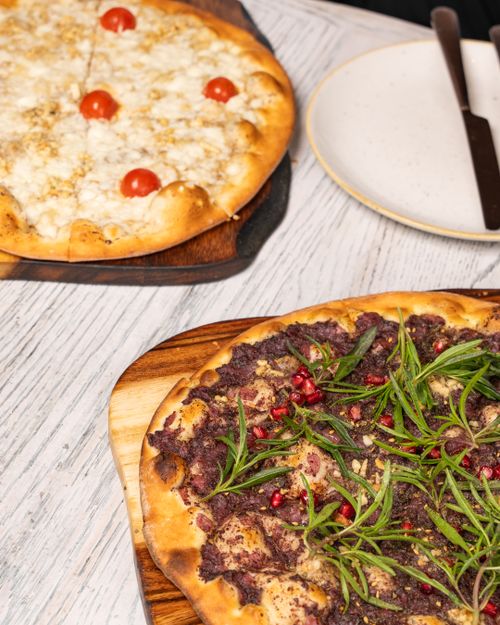 Free Delicious gourmet pizzas topped with fresh herbs and cherry tomatoes on a wooden cutting board. Stock Photo