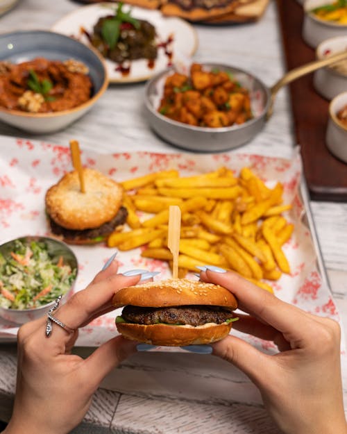 A person holding a burger and fries in front of a table
