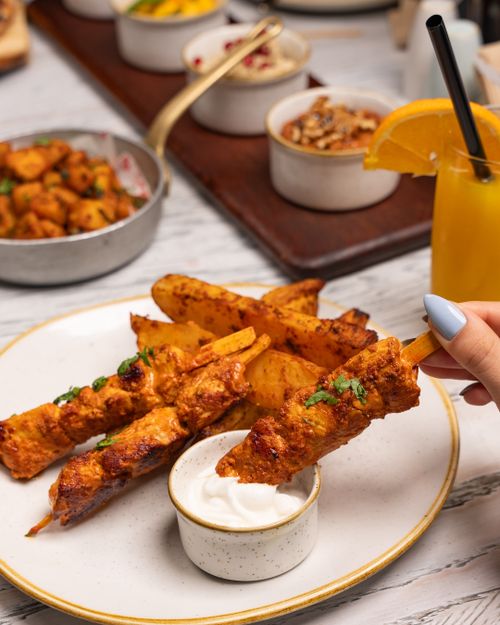 Free Enjoy a mouthwatering chicken skewers meal served with dips and wedges at a cozy restaurant. Stock Photo