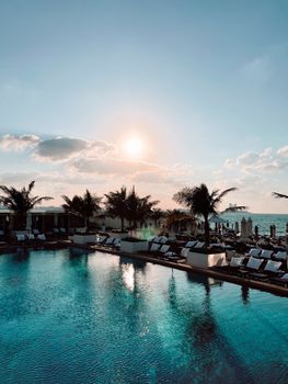 Luxurious resort pool with palm trees and sun loungers under a summer sunset.