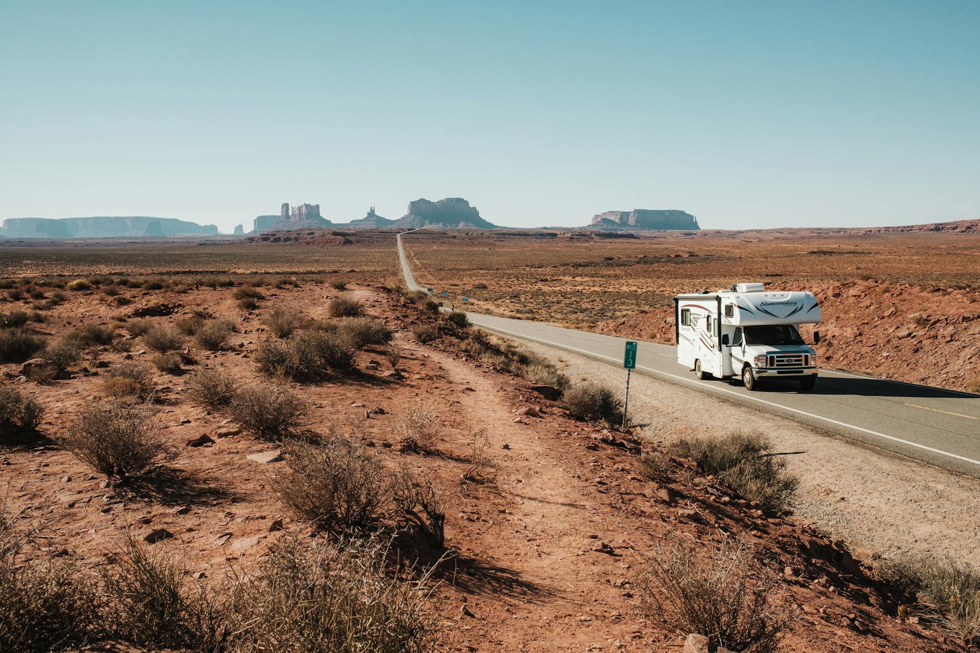 An RV travels along a deserted road in Monument Valley, capturing breathtaking rock formations and vast arid landscape.