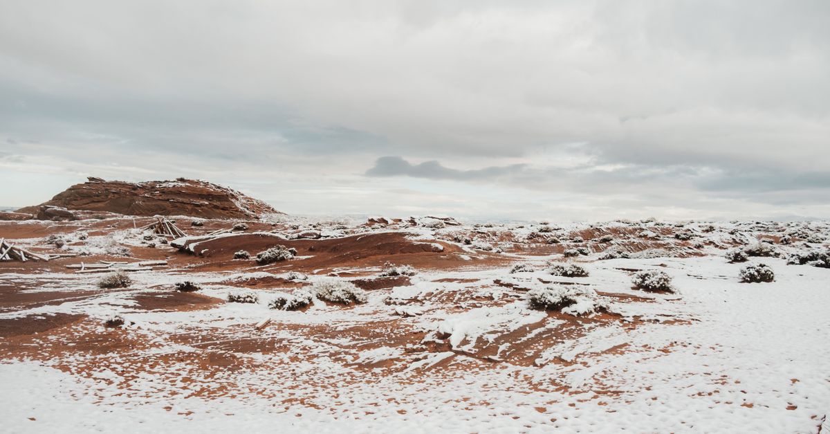 A serene desert landscape with a light snow covering under an overcast sky in Arizona.