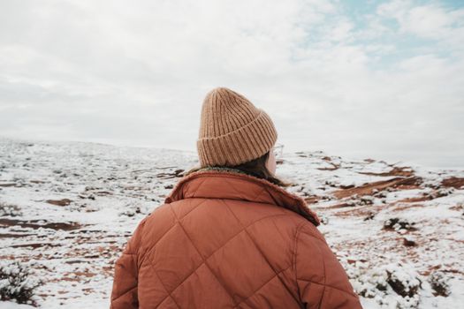 A person in a coat and beanie explores a snowy desert landscape, showcasing adventure and seasonal contrast.
