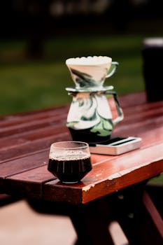 A serene outdoor coffee scene featuring a pour-over setup on a rustic wooden table.