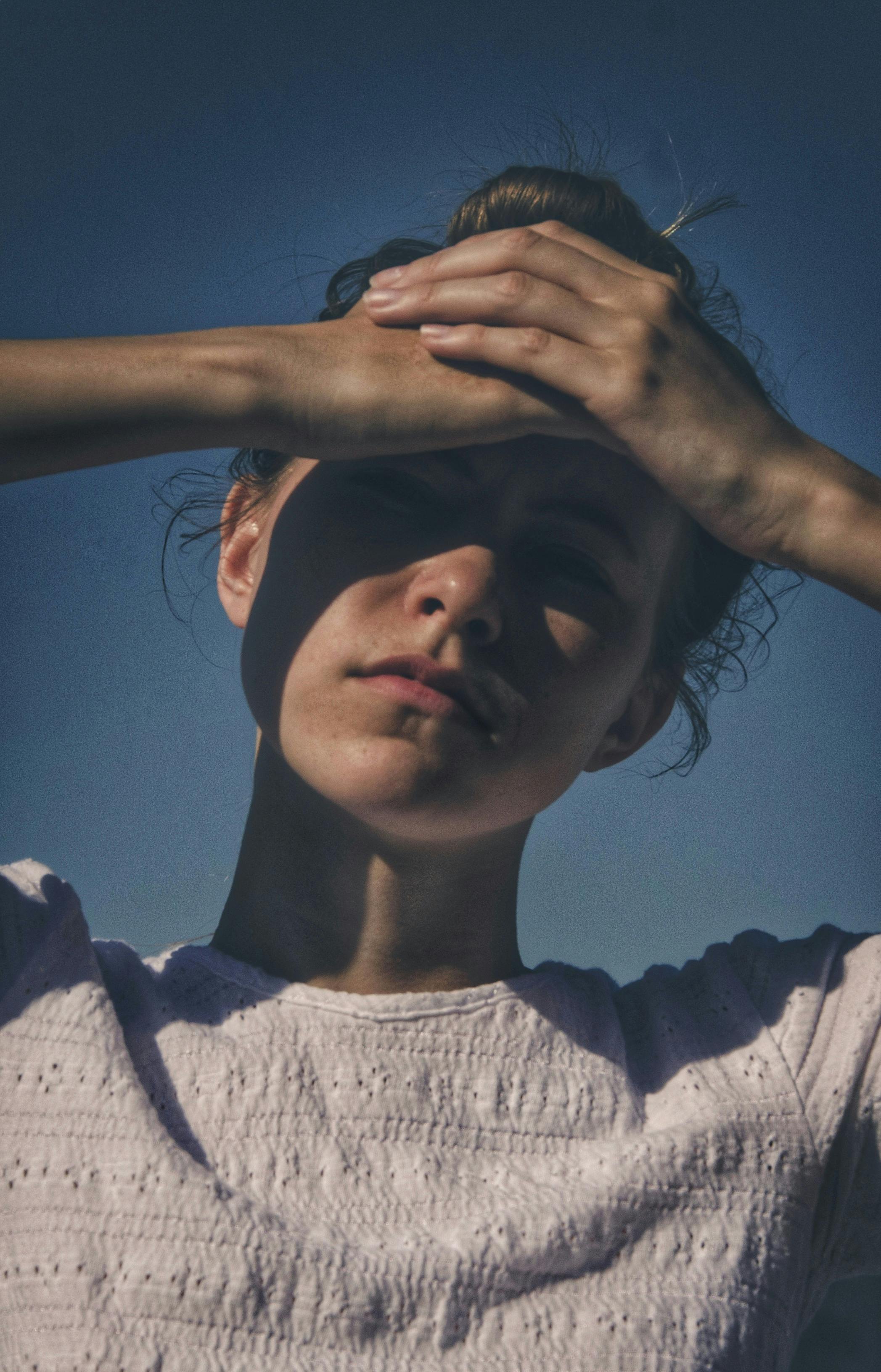 一位女性用手遮挡阳光，在脸上投下戏剧性的阴影