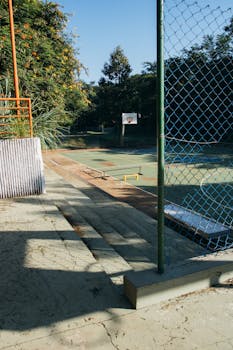 An empty outdoor basketball court on a sunny day surrounded by greenery.