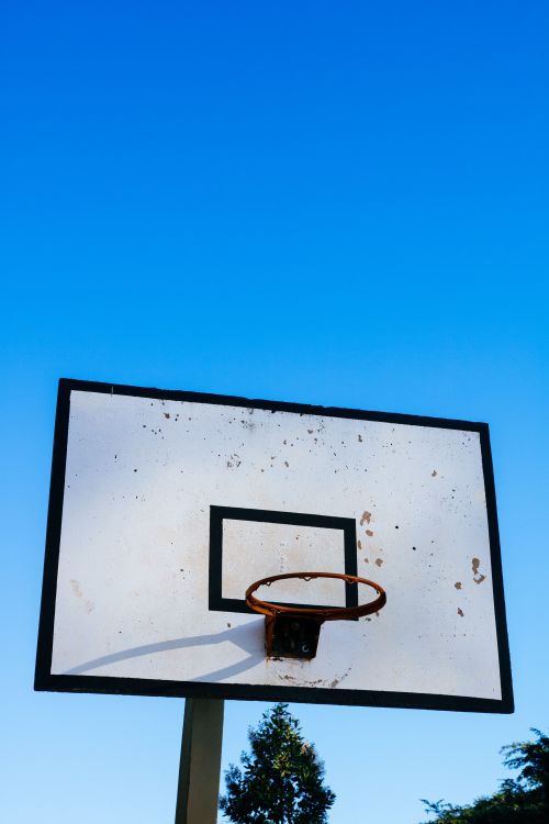 Free A rustic basketball hoop and backboard under a clear blue sky, ideal for sport-themed visuals. Stock Photo