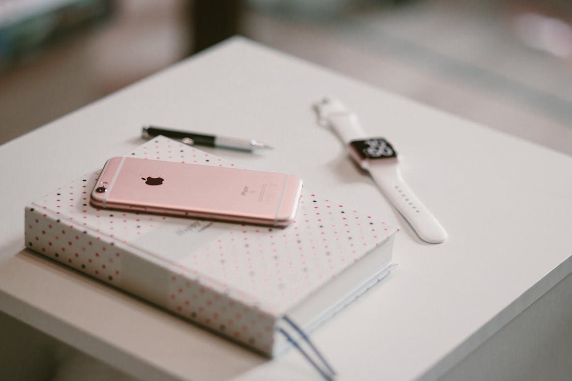 Free Rose Gold Iphone 6 S on Top of White Covered Book Stock Photo