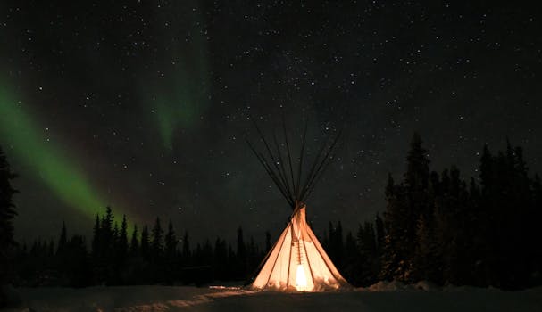 Stunning aurora borealis illuminating a teepee under a starry sky in Yellowknife, Canada.