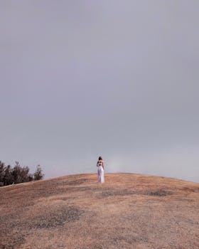 一位孤独的女子站在山顶，头顶是广阔晴朗的天空，她捕捉到了那份平静的孤寂
