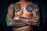 一个赤裸上身的男人的特写，他有着彩色袖子纹身和胸部艺术
