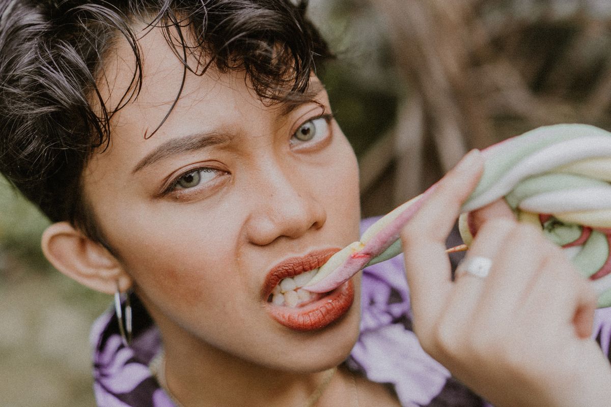 Person biting into colorful candy rope outdoors with a focused expression. Captivating moment.