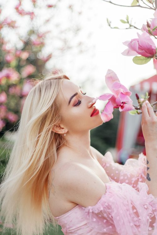 Free Blonde woman enjoying pink blossoms in a spring garden, capturing elegance and beauty. Stock Photo