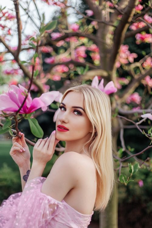 Free A beautiful woman with blonde hair stands serenely amidst vibrant spring blossoms outdoors. Stock Photo