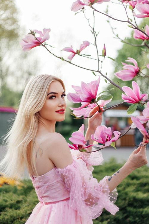 Free A beautiful woman in a pink dress standing among vivid spring blossoms in a garden. Stock Photo
