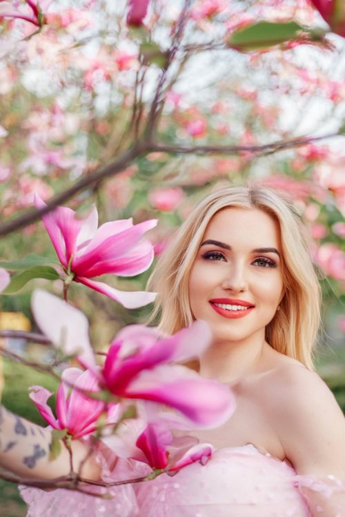 Free Blonde woman smiling amid blooming magnolias in spring garden, showcasing natural beauty Stock Photo