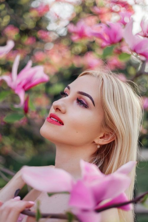 Free A woman with blonde hair poses gracefully amongst vibrant pink magnolia flowers in bloom. Stock Photo