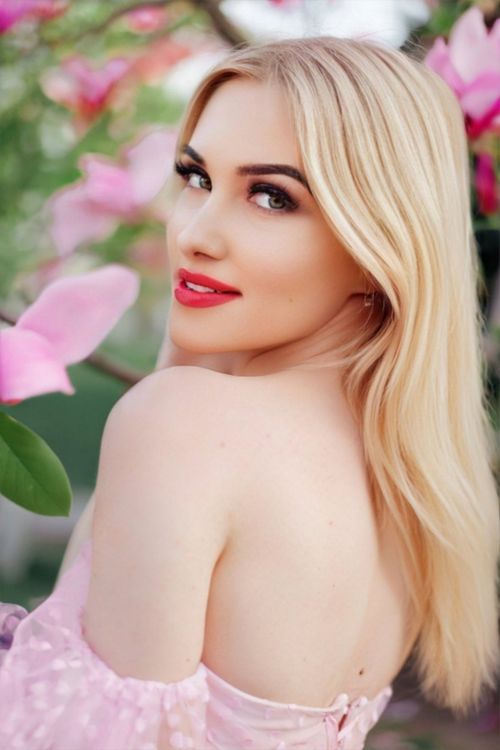 Free A glamorous portrait of a blonde woman posing among pink flowers, showcasing elegance and beauty. Stock Photo
