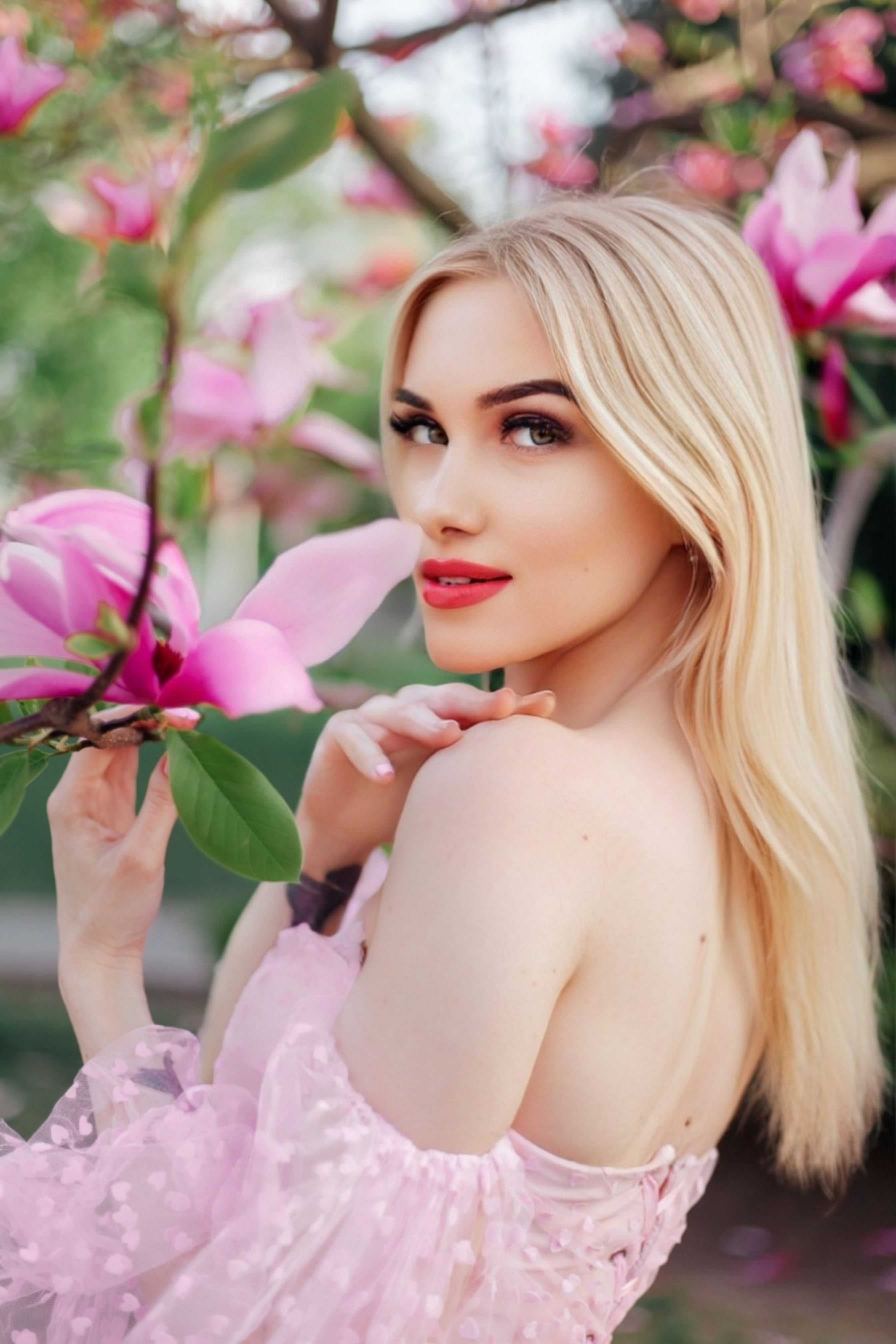 Blonde woman in a pink dress surrounded by magnolia flowers. Captures natural beauty and elegance.
