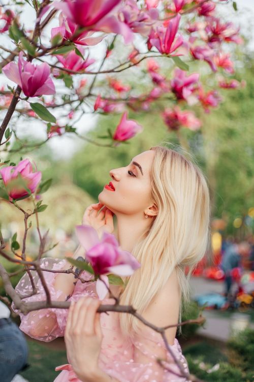 Free Elegant blonde woman enjoying the vibrant spring blossoms in a garden. Stock Photo