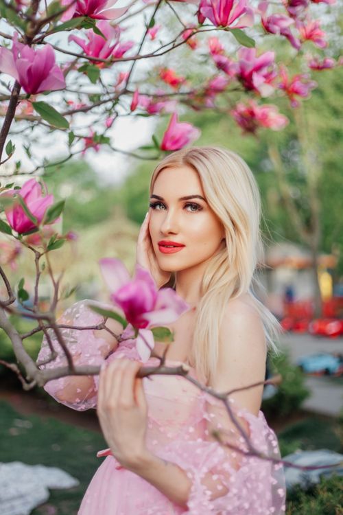 Free Blonde woman in a pink dress posing gracefully among blooming magnolia branches, embodying spring's charm. Stock Photo