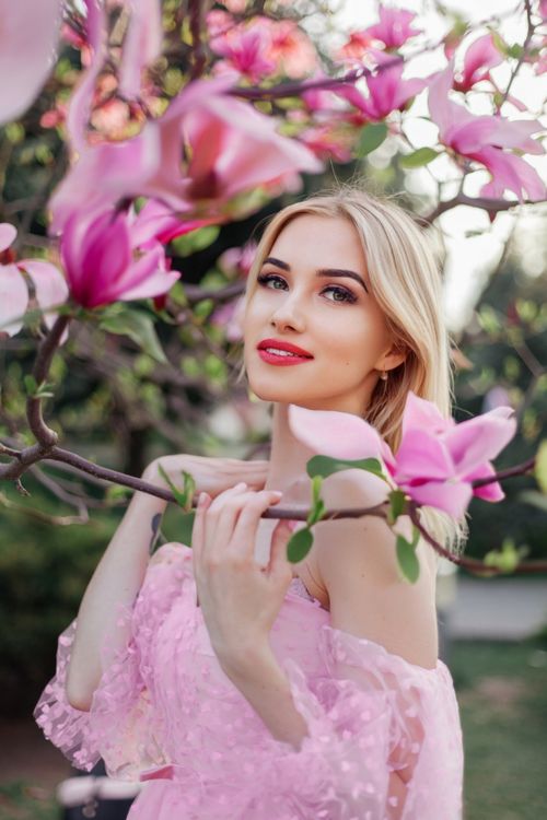 Free A woman in a pink dress stands among vibrant magnolia blossoms outdoors. Stock Photo