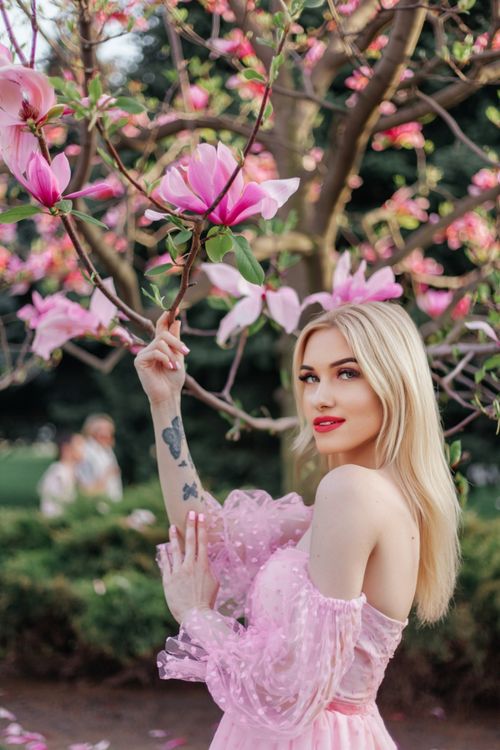 Free A blonde woman in a pink dress poses amidst blooming magnolias in spring. Stock Photo