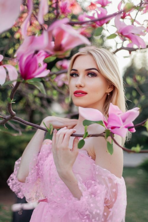 Free Blonde woman in pink dress posing with magnolia blooms. Soft, natural outdoor setting. Stock Photo