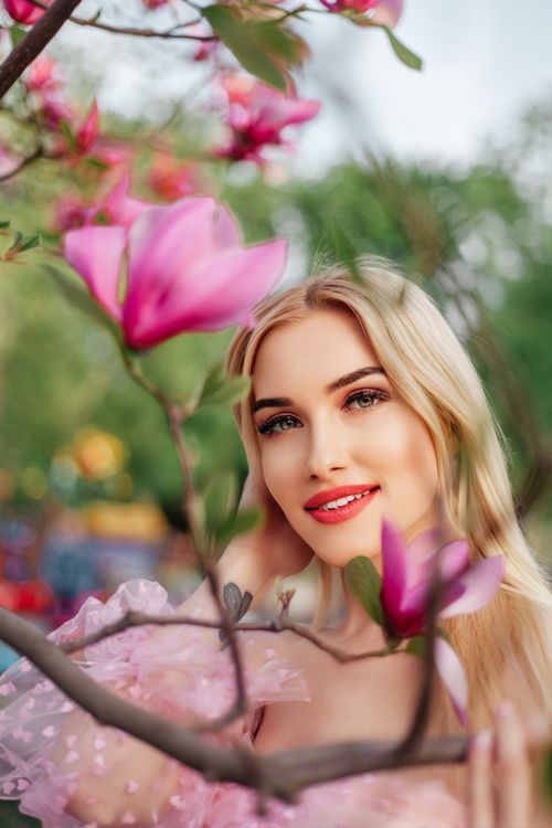 Free Blonde woman smiling amidst vibrant magnolia blossoms, capturing the essence of spring. Stock Photo