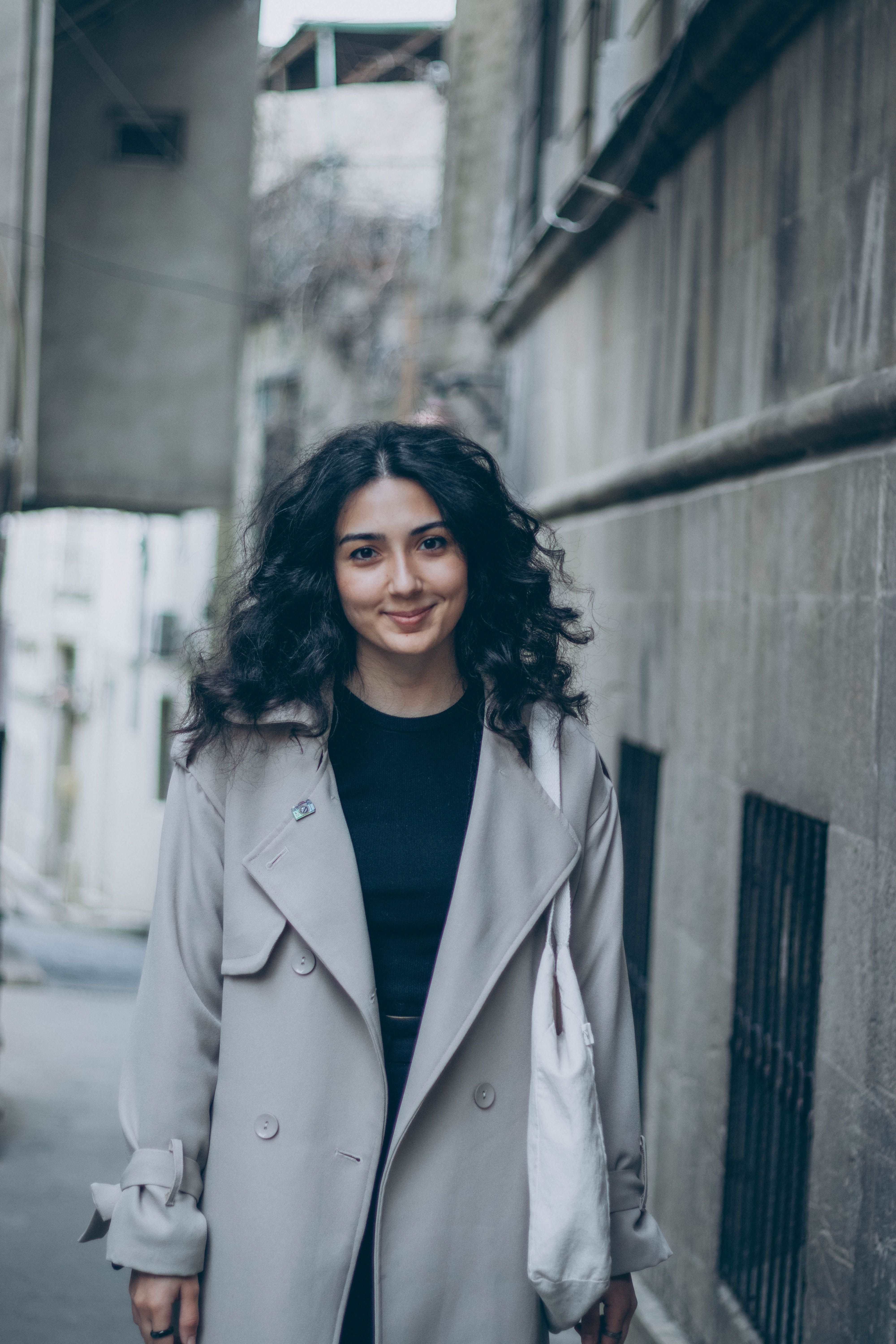 Young woman in a stylish coat smiling while walking through the historic streets of Baku, Azerbaijan.