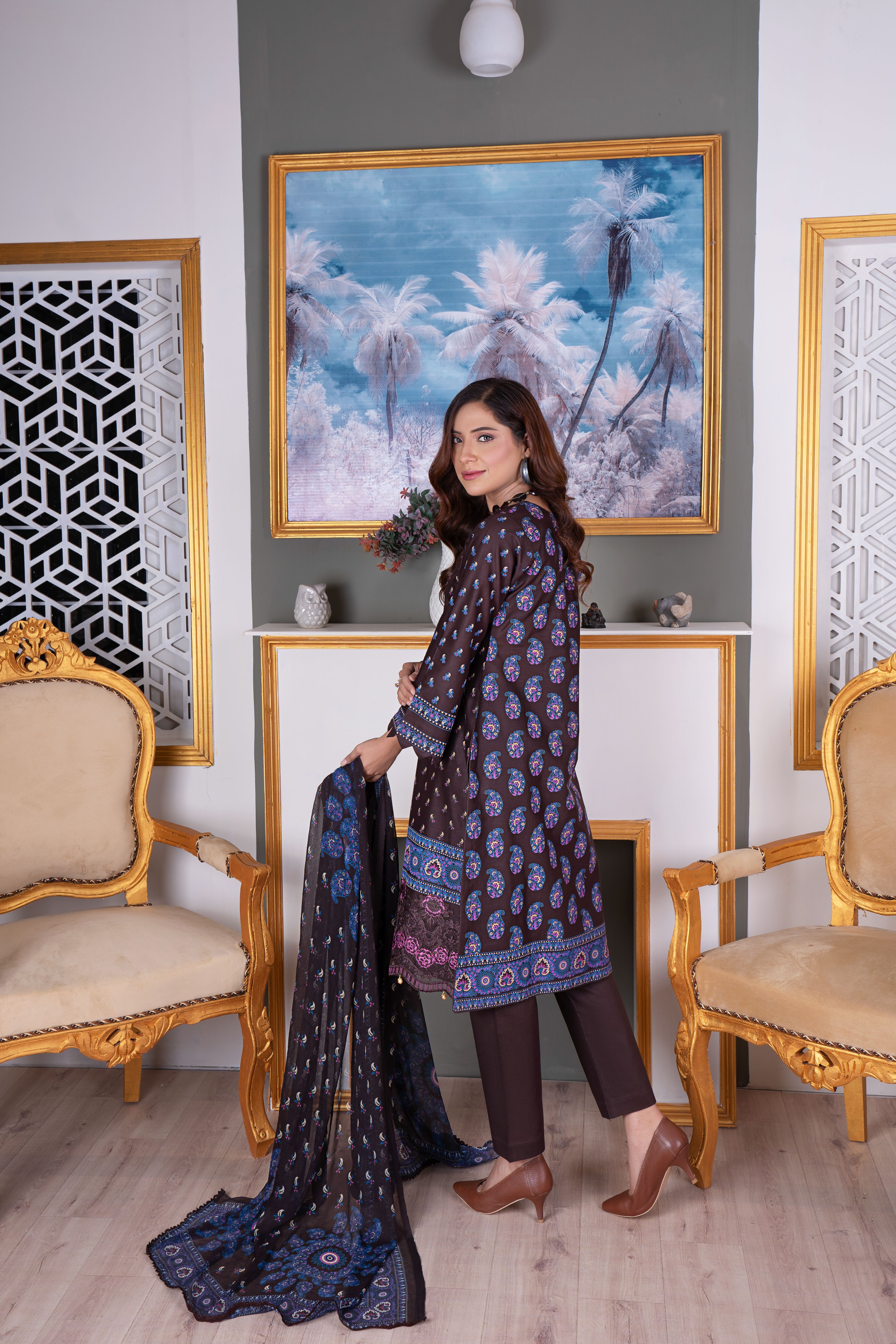Portrait of a woman in ethnic attire standing indoors with elegant furnishings and artwork.