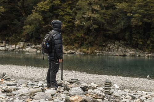 Free Hiker by a peaceful river, bundled for winter adventure in lush nature. Stock Photo