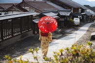 一位穿着和服的妇女撑着红伞，走过日本传统村庄的街道