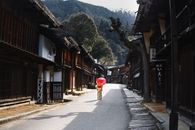 在日本风景优美的乡村街道上，一名身着和服的女子撑着红伞，捕捉到了文化的精髓