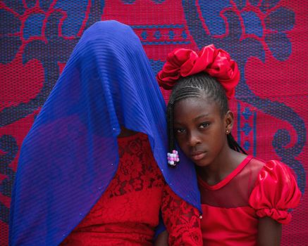 Woman Covered with a Blue Scarf and a Teenager in Red Dresses