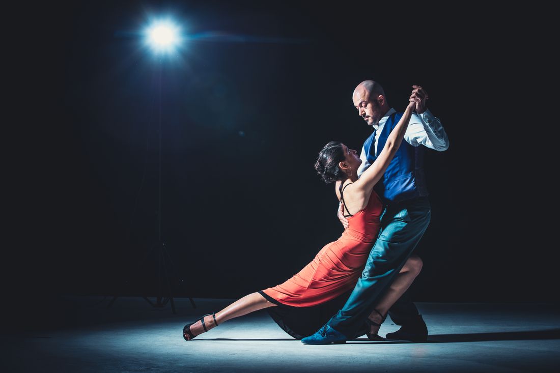 Pareja bailando tango bajo un foco, ella con vestido rojo