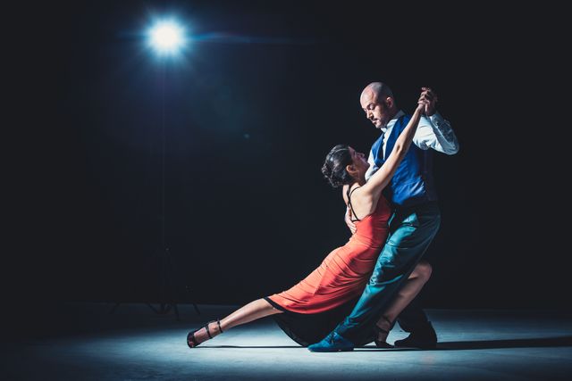 Pareja bailando tango bajo un foco, ella con vestido rojo