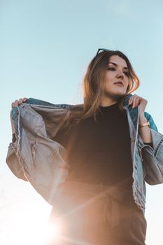 一位穿着牛仔夹克的时尚女性，以阳光和蓝天为背景