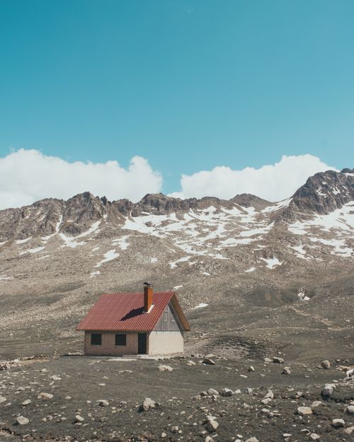 Free A solitary cabin in a snowy mountainous landscape under a clear blue sky, capturing serene beauty. Stock Photo