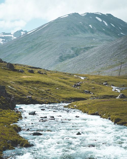 Free A beautiful summer landscape featuring a river flowing through mountains under a cloudy sky. Stock Photo