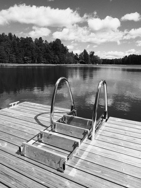 Black and white photo of a tranquil jetty in Porvoo, Finland, with reflections on a calm lake.