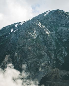 A rugged mountain peak with snow patches under a cloudy sky, offering a dramatic landscape view.