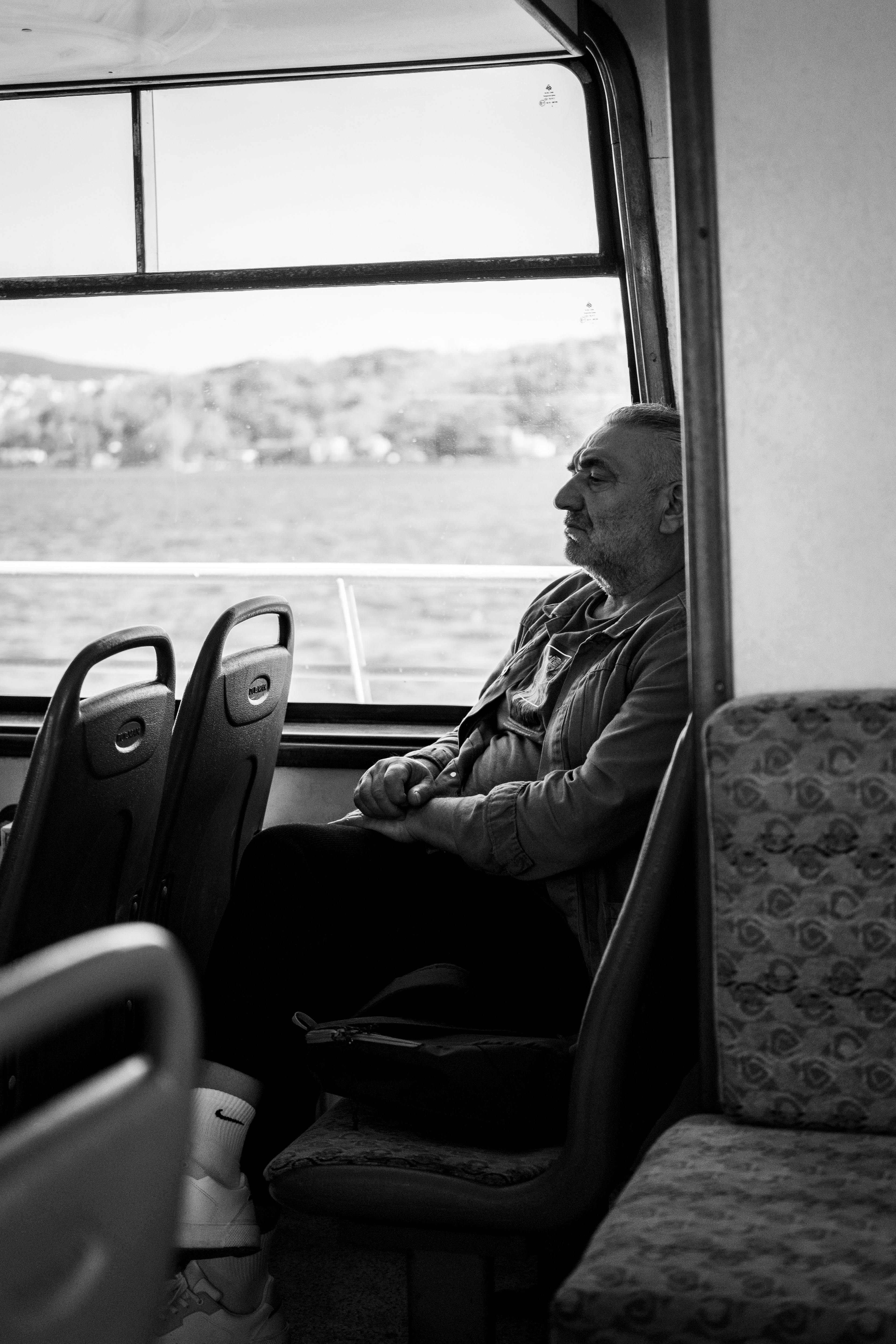 A senior man sits alone on a train, gazing out the window in contemplation.
